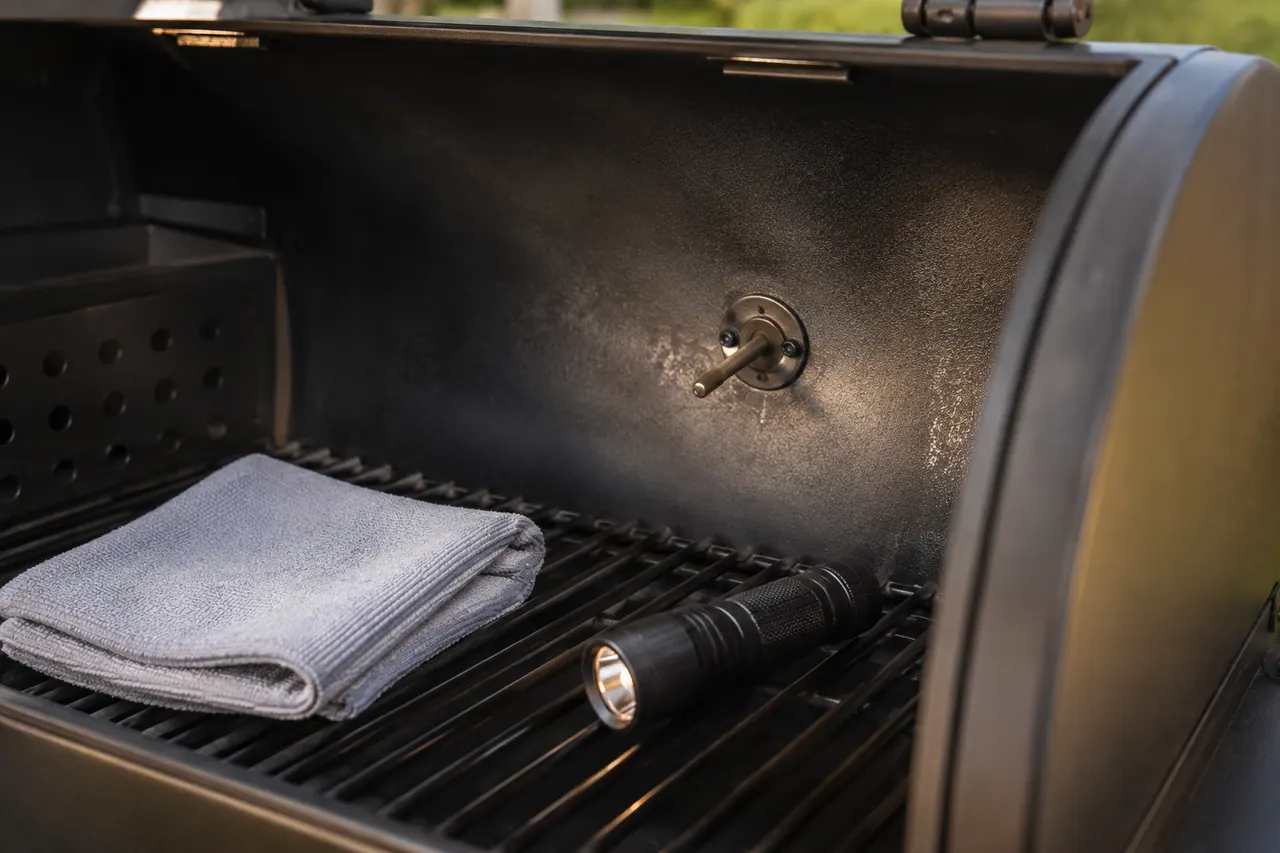 A fixed cooker temperature sensor inside a cool unbranded pellet grill with a cloth and flashlight nearby.