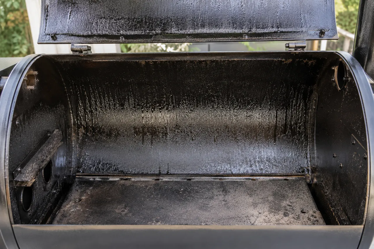 The inside of a cold unbranded pellet grill with a dark, tar-like residue on the lid and barrel walls.