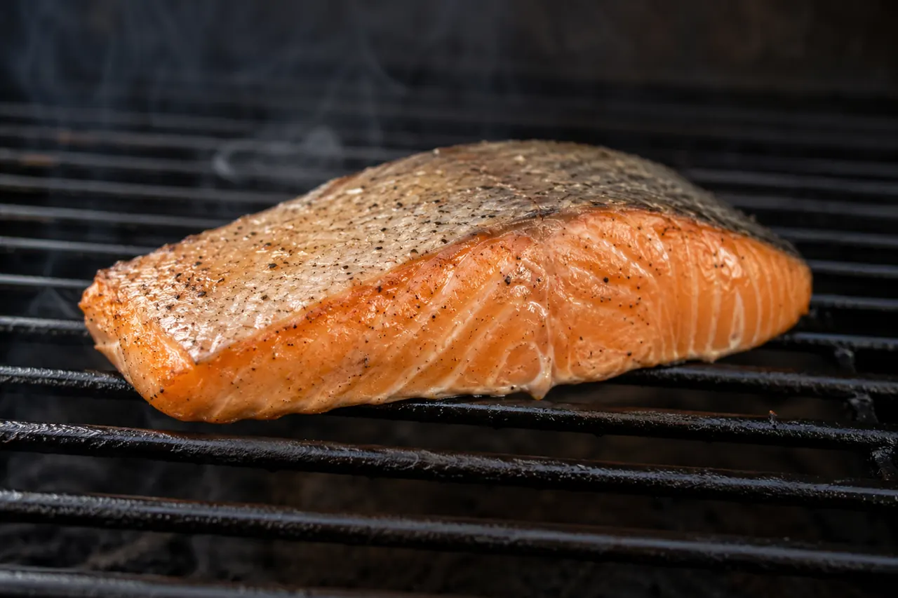 A thick salmon fillet cooking on a clean unbranded pellet grill grate.