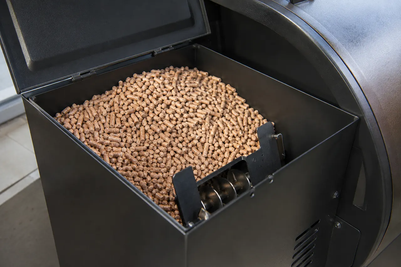 A clean pellet grill hopper with dry wood pellets flowing toward the visible auger opening.
